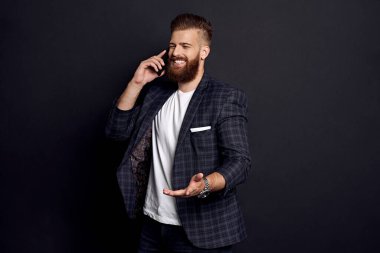 Seni duyduğuma çok sevindim. Yakışıklı genç adam, siyah arka planda dururken gülümseyerek telefonunu kullanıyor.