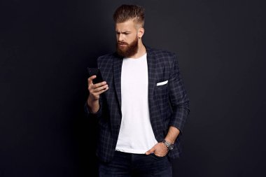 Arkadaşlardan mesajlar alıyorum. Yakışıklı genç adam akıllı telefon kullanıyor ve siyah arka planda dururken gülümsüyor..