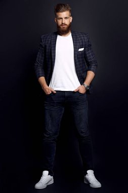 Kendinden emin ve yakışıklı. Zencefilli sakallı, şık giyinmiş, siyah arka planda poz verirken kameraya bakan genç bir adam..