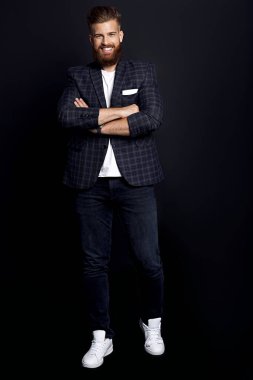 Kendinden emin ve yakışıklı. Zencefilli sakallı, şık giyinmiş, siyah arka planda poz verirken kameraya gülümseyen genç bir adam..