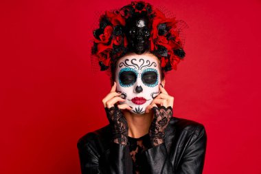 Genç, tüyler ürpertici bayan Calavera. Ölülerin ziyafeti için sanatsal makyaj yapıyor. Kafasında çiçek çelengi olan siyah deri bir ceket giymişti. Ölüler Günü 'nün sembolü kırmızıyla izole edilmişti.