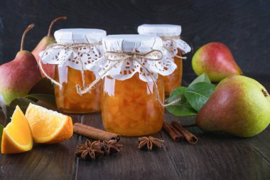 Armut ve turuncu olgun armut, tarçın, anason yıldız ve masada yeşil yaprakları ile Cam Kavanoz reçel.