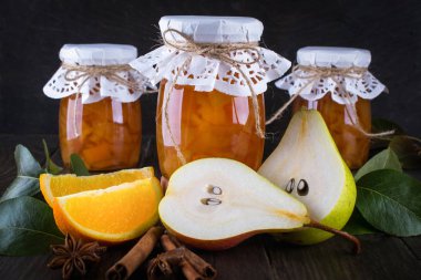 Armut ve turuncu olgun armut, tarçın, anason yıldız ve masada yeşil yaprakları ile Cam Kavanoz reçel.