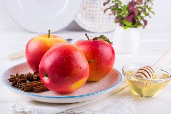 Fresh, ripe organic  sweet apple in dish with cinnamon sticks, anise stars and honey on a white kitchen table.