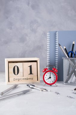 1 Eylül. Ahşap takvim, okul malzemeleri Grup, gri bir tablo üzerinde kırmızı çalar saat. Geri okul kavramı.