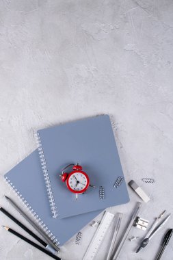 Gri dizüstü bilgisayarlar ve büro malzemeleri, beton zemin üzerine kırmızı çalar saat. Okula dönüş.