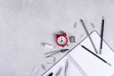 Gri dizüstü bilgisayarlar ve büro malzemeleri, beton zemin üzerine kırmızı çalar saat. Okula dönüş.