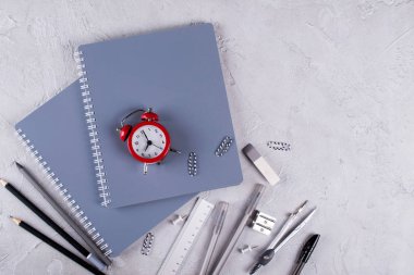 Gri dizüstü bilgisayarlar ve büro malzemeleri, beton zemin üzerine kırmızı çalar saat. Okula dönüş.