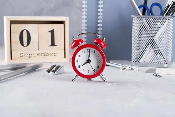 1 Eylül. Ahşap takvim, okul malzemeleri Grup, gri bir tablo üzerinde kırmızı çalar saat. Geri okul kavramı.