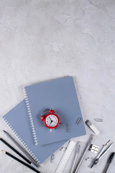 Gri dizüstü bilgisayarlar ve büro malzemeleri, beton zemin üzerine kırmızı çalar saat. Okula dönüş.