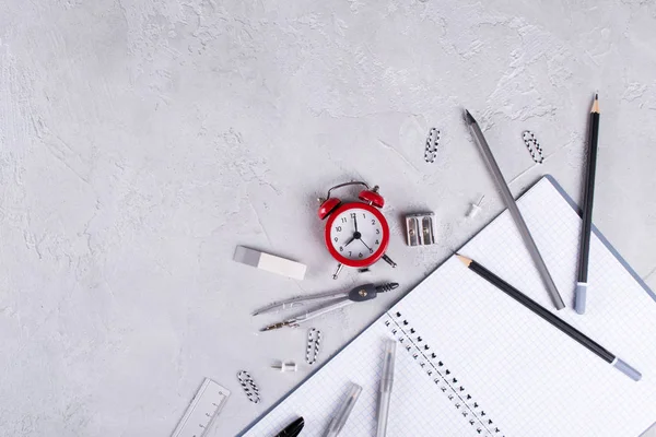 Gri dizüstü bilgisayarlar ve büro malzemeleri, beton zemin üzerine kırmızı çalar saat. Okula dönüş.