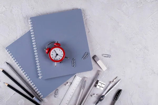 Gri dizüstü bilgisayarlar ve büro malzemeleri, beton zemin üzerine kırmızı çalar saat. Okula dönüş.