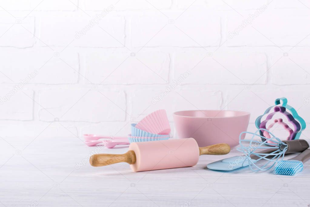 Baking background with kitchen tools: rolling pin, wooden spoons, whisk, sieve, bakeware and shape cookie cutter on white wooden background.
