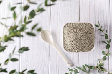 Yeşil kil tozu ve taze okaliptüs ile seramik kase beyaz zemin üzerine bırakır. Yüz ve vücut bakım kavramı.