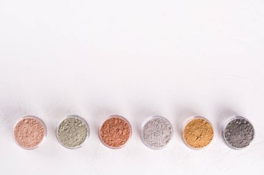 Beyaz arkaplanda farklı kozmetik çamur tozları.