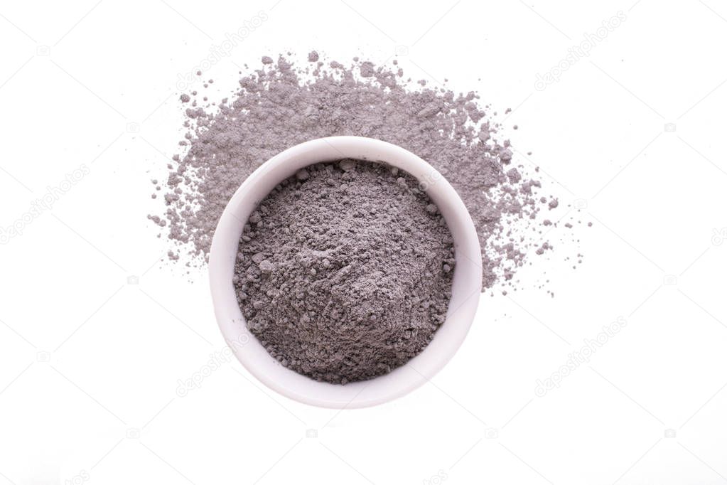 Dry black clay powder mask for face and body  in ceramic bowl isolated on white