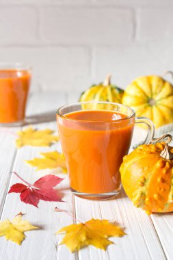 Geleneksel sonbahar içki. Cam bardak kabak suyu, kabak ve düşmüş akçaağaç yaprakları