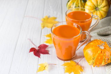 Taze kabak suyu cam fincan, kabak ve düşmüş akçaağaç yaprakları. Sonbahar içecek konsepti