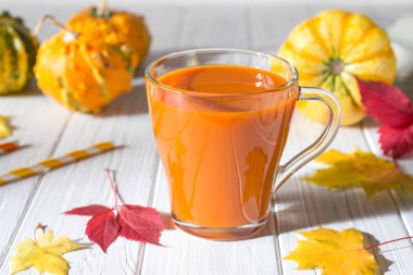 Taze kabak suyu cam fincan, kabak ve düşmüş akçaağaç yaprakları. Sonbahar içecek konsepti