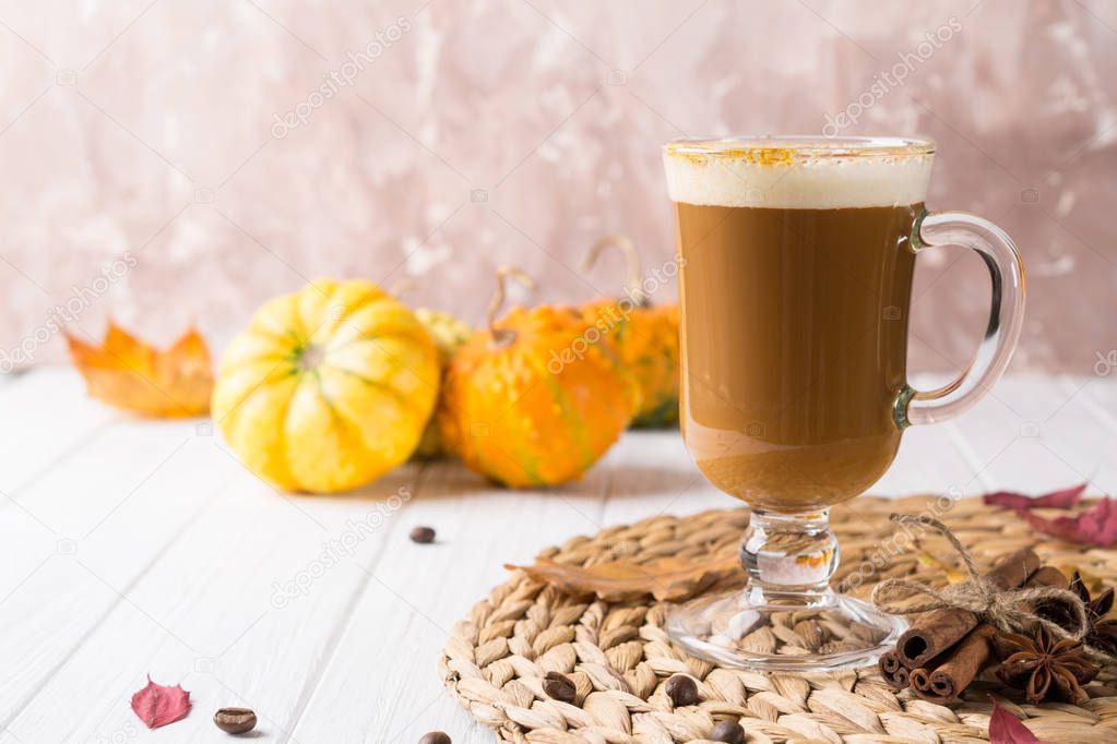 Pumpkin spiced latte or coffee in glass cup, dry leaves. Traditional autumn or winter hot drink. Space for text