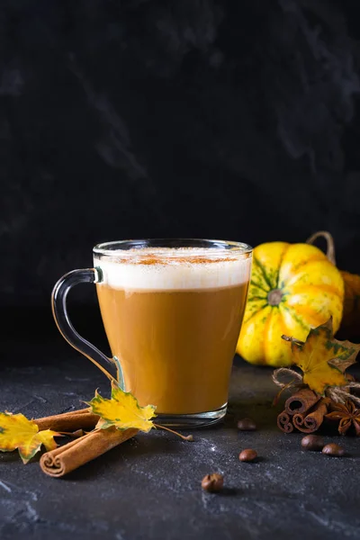 Pumpkin spiced latte or coffee in glass cup, dry leaves. Traditional autumn or winter hot drink. Space for text