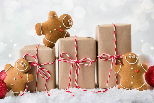 Packing Christmas gifts.  Three Christmas gift boxes wrapped in kraft paper tied with red and white string and three smiling  gingerbread men cookies on white winter background. copy space