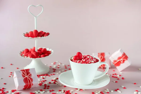 Festive background.  Coffee cup, white two tier serving tray full of multicolor sweet sprinkles sugar candy hearts and packing Valentine\'s  Day gifts  Love and Valentine\'s day concept.