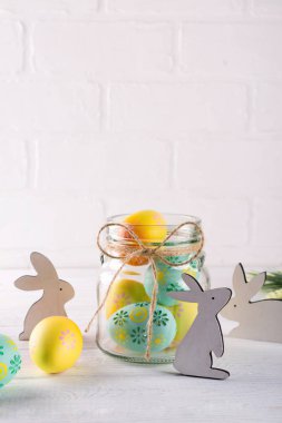 Ev yapımı Paskalya dekor ile kompozisyon. Cam kavanoz renkli Paskalya yumurtaları ve ahşap tavşan ile. Beyaz arka plan üzerinde