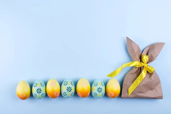 Easter holiday background with eggs. Top view of colorful painted chicken eggs plased  in a row and  craft paper package in the shape of bunny