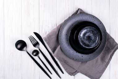 Porselen el sanatları gri ve siyah plakalar ve kase çatal ayarlayın, bir beyaz tahta masada keten peçete. Düz yatıyordu