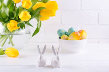 Cam vazoda Sarı Lale çiçek ve beyaz arka plan üzerinde iki beyaz seramik tavşan buket ile Paskalya kompozisyon