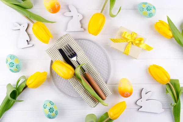 Spring Easter background for menu. Easter egg decoration, bunny, linen  napkin on plate and  kitchen cutlery on white wooden table. Flat lay
