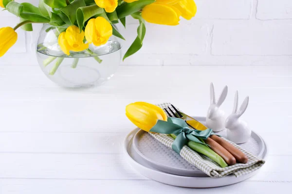 Spring Easter background for menu. Easter egg decoration, bunny, linen  napkin on plate and  kitchen cutlery on white wooden table.