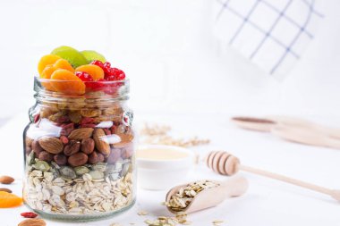 Cam Kavanoz malzemelerle granola beyaz arka plan üzerinde yemek pişirmek için. Yulaf gevreği, tatlım, fındık, Kuru Meyve ve tohumlar. Sağlıklı snak