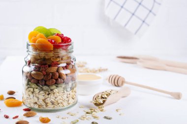 Cam Kavanoz malzemelerle granola beyaz arka plan üzerinde yemek pişirmek için. Yulaf gevreği, tatlım, fındık, Kuru Meyve ve tohumlar. Sağlıklı snak