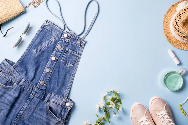 Flat lay  woman summer clothes and accessories collage on blue with jeans overalls, glasses, sneakers, handbag, wicker hat,