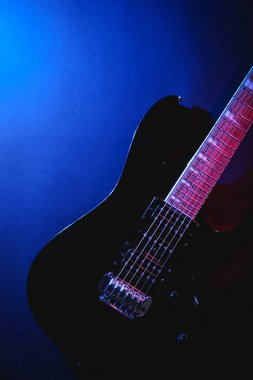 Kopya alanı ile siyah bir arka plan üzerinde elektrik modern siyah gitar üst görünümü. Renkli mavi ve mor doğal aydınlatma ile. 