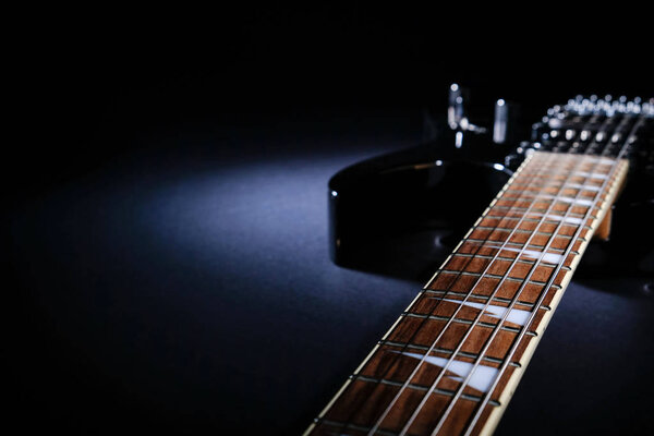 Modern black electric guitar. Close-up of fingerboard under beam of light. With copy space