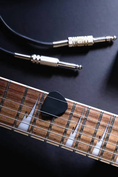 Guitar frets with strings and mediator, jack cable on dark background