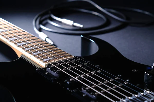 黒の背景にジャックケーブルと現代の黒のエレキギター — ストック写真