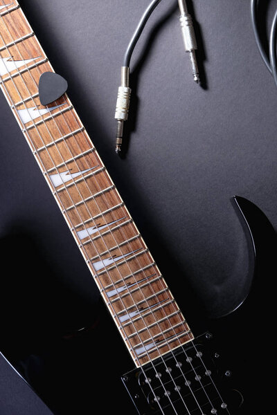 Modern black electric guitar with jack cable on black background