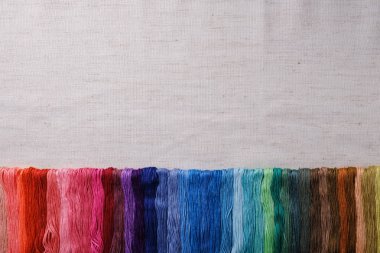 Nakış için renkli iplikler. Tuval arka planda üst üste dizilmiş çok renkli iş parçacığı. Bir mockup üst görünümü