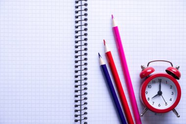 Okul zamanı minimalist kavramı. Renkli kalemler, defterler ve kırmızı çalar saat. Üstte görüntü 