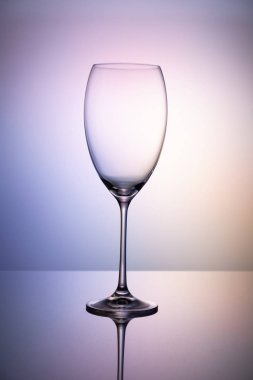 İnce bir bacak üzerinde şarap olmadan boş cam kadeh bir ayna yüzeyinde duruyor. Renkli mor arka plan.