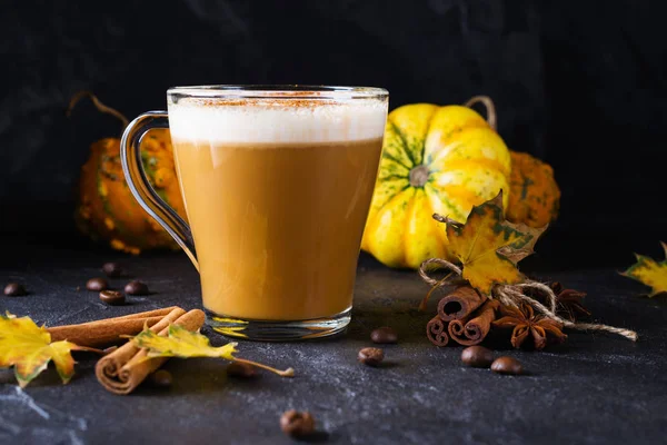 Pumpkin spiced latte or coffee in glass cup, dry leaves. Traditional autumn or winter hot drink.