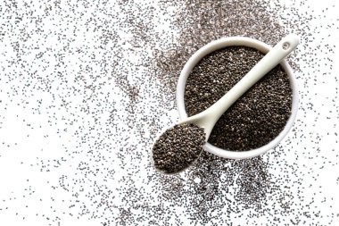 Beyaz arka planda beyaz seramik kase ve kaşık içerisindeki Chia tohumları (Salvia hispanica). Sağlıklı yiyecek ya da süper yiyecek ve destek konsepti. Düz yatıyordu.