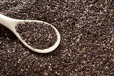 Beyaz seramik kaşıkta Chia tohumları bir tohum yığınının üstünde.. 