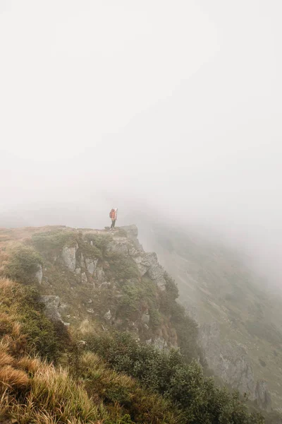 man stands on the edge of the mountain in a fog