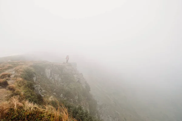 man stands on the edge of the mountain in a fog