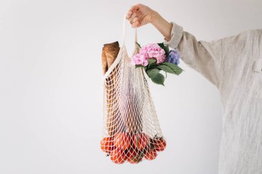 Domates, ekmek ve çiçek ile dize alışveriş çantası tutan kadın el. Ekoloji kavramı, çevre koruma. Sıfır atık.